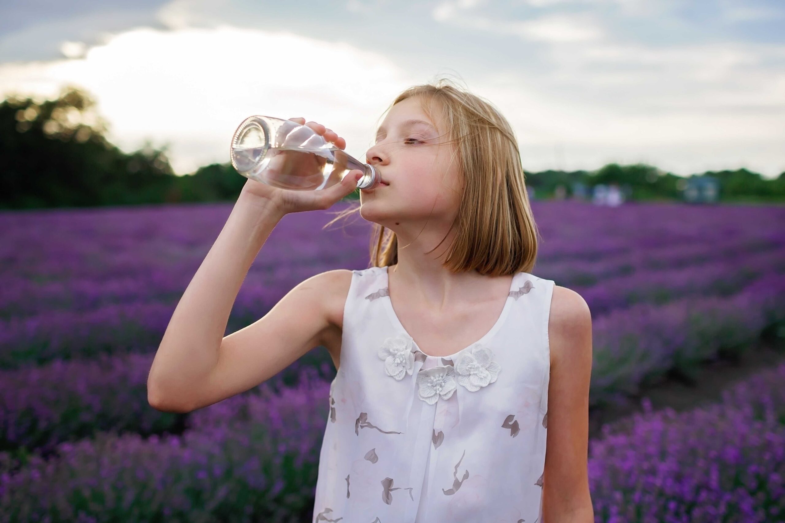 a teenage girl drinking water from glass bottle